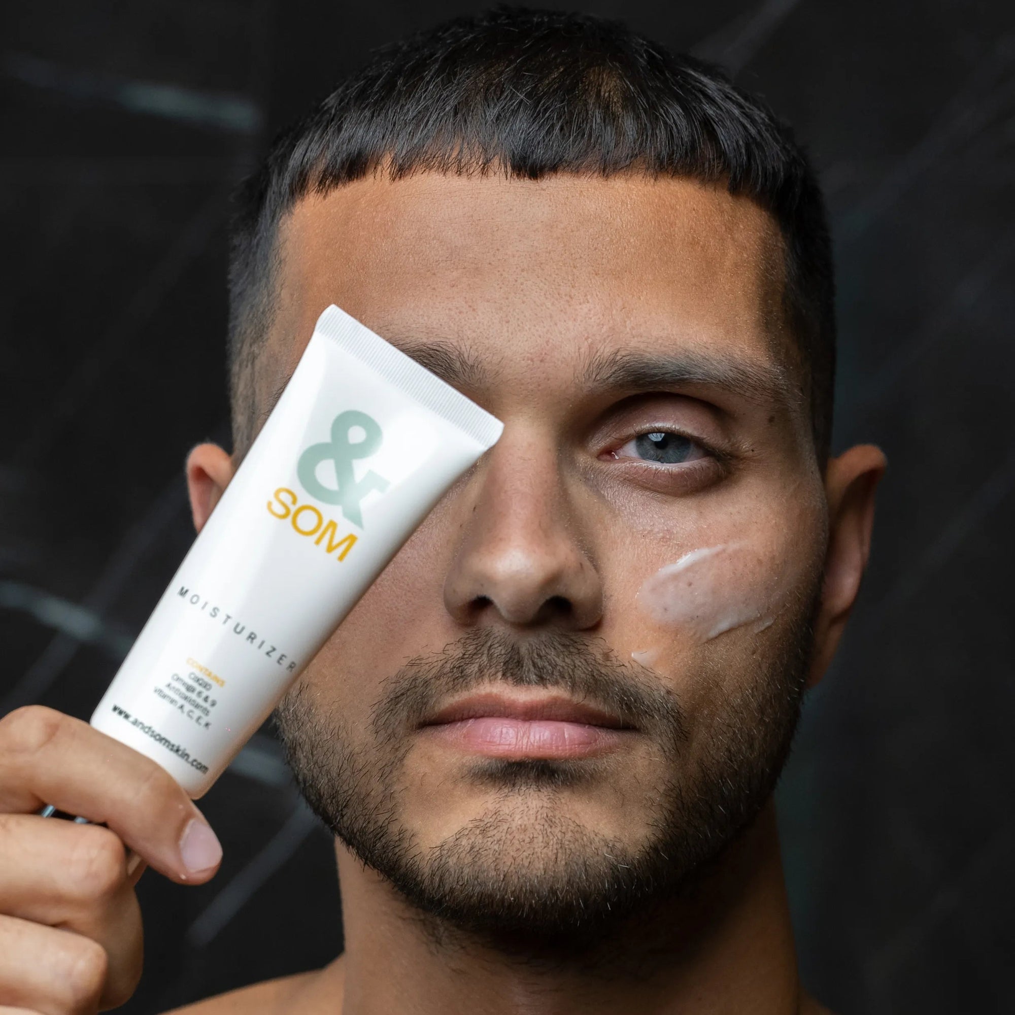 Man holding a skincare product with a brand logo against a dark background
